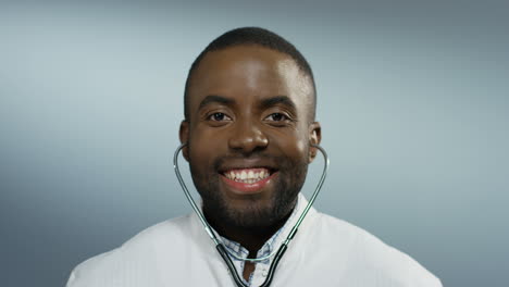 Portrait-of-the-young-attractive-African-American-man-physician-with-stethoscope-in-ears-smiling-joyfully-to-the-camera.-Close-up.